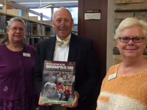 Mike Harmless presents a copy of Donald Davidson's Autocourse Official Illustrated History of the Indianapolis 500 to Becky Kelien (left) and Libby Pollard (right).