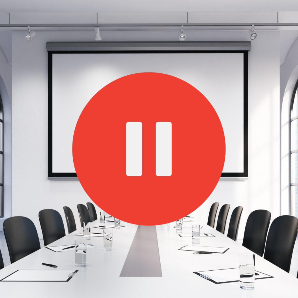 photograph of meeting room with a red circle in the center containing a pause button